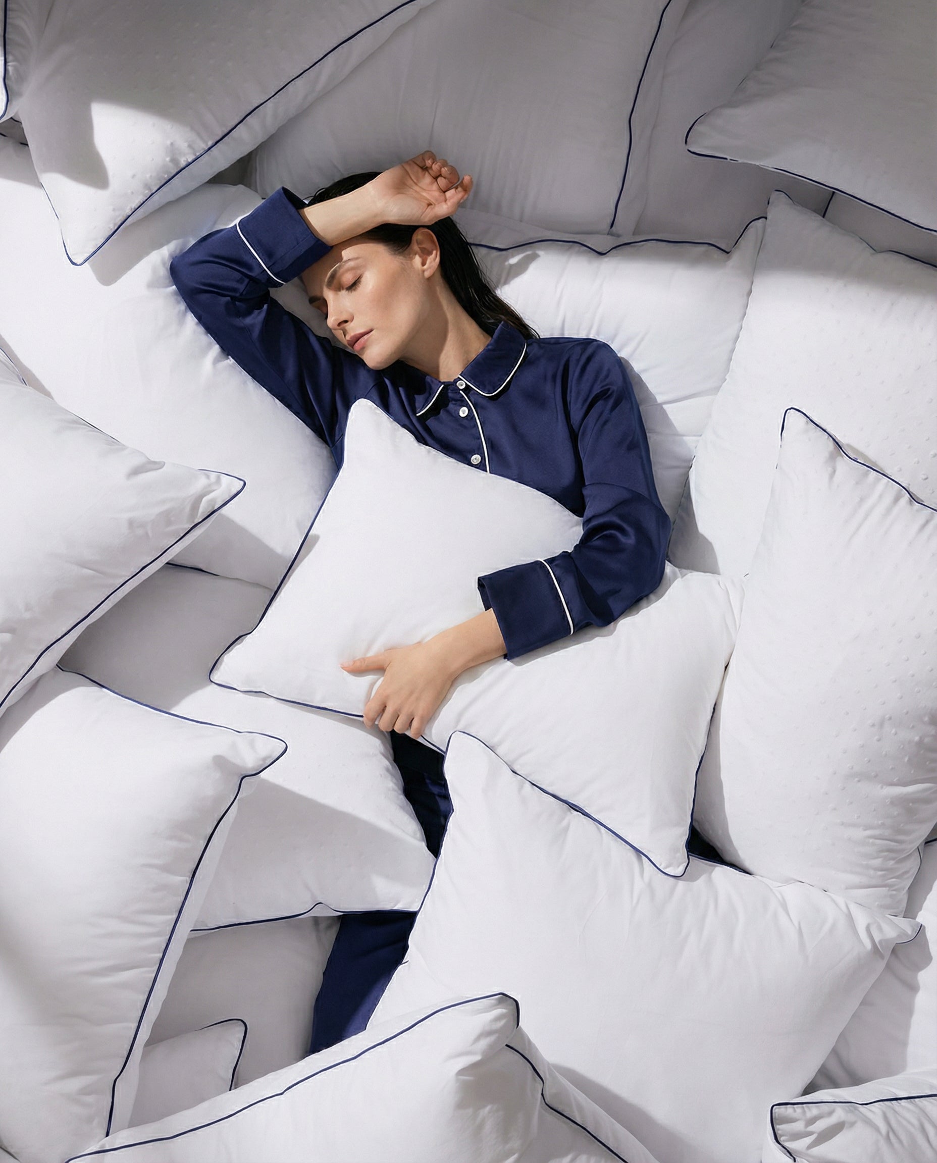 Woman with SELENEY MIDnight blue pajama surrounded by soft, fluffy cushions. 